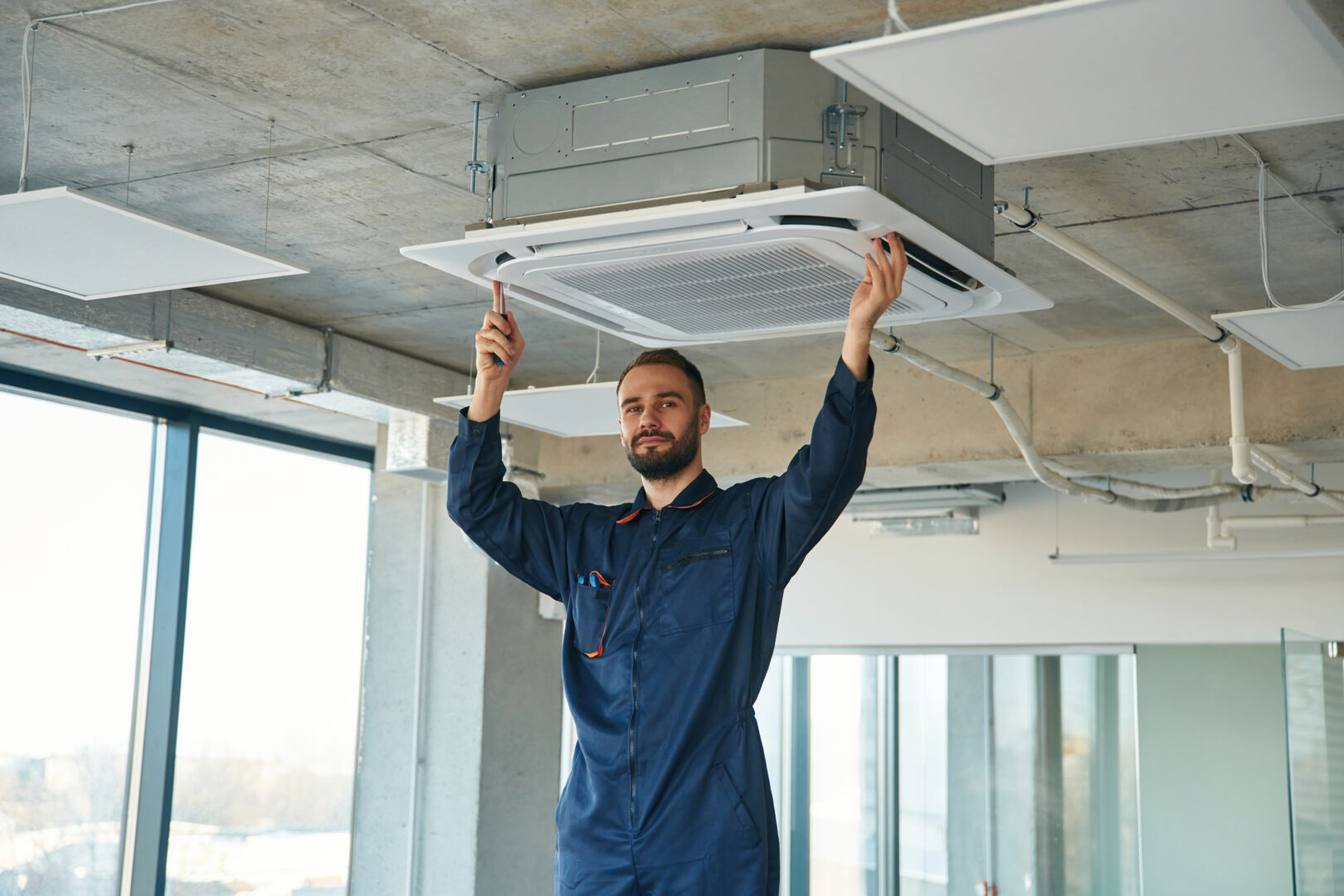A man repairs the ventilation system, the device hangs on the ceiling.