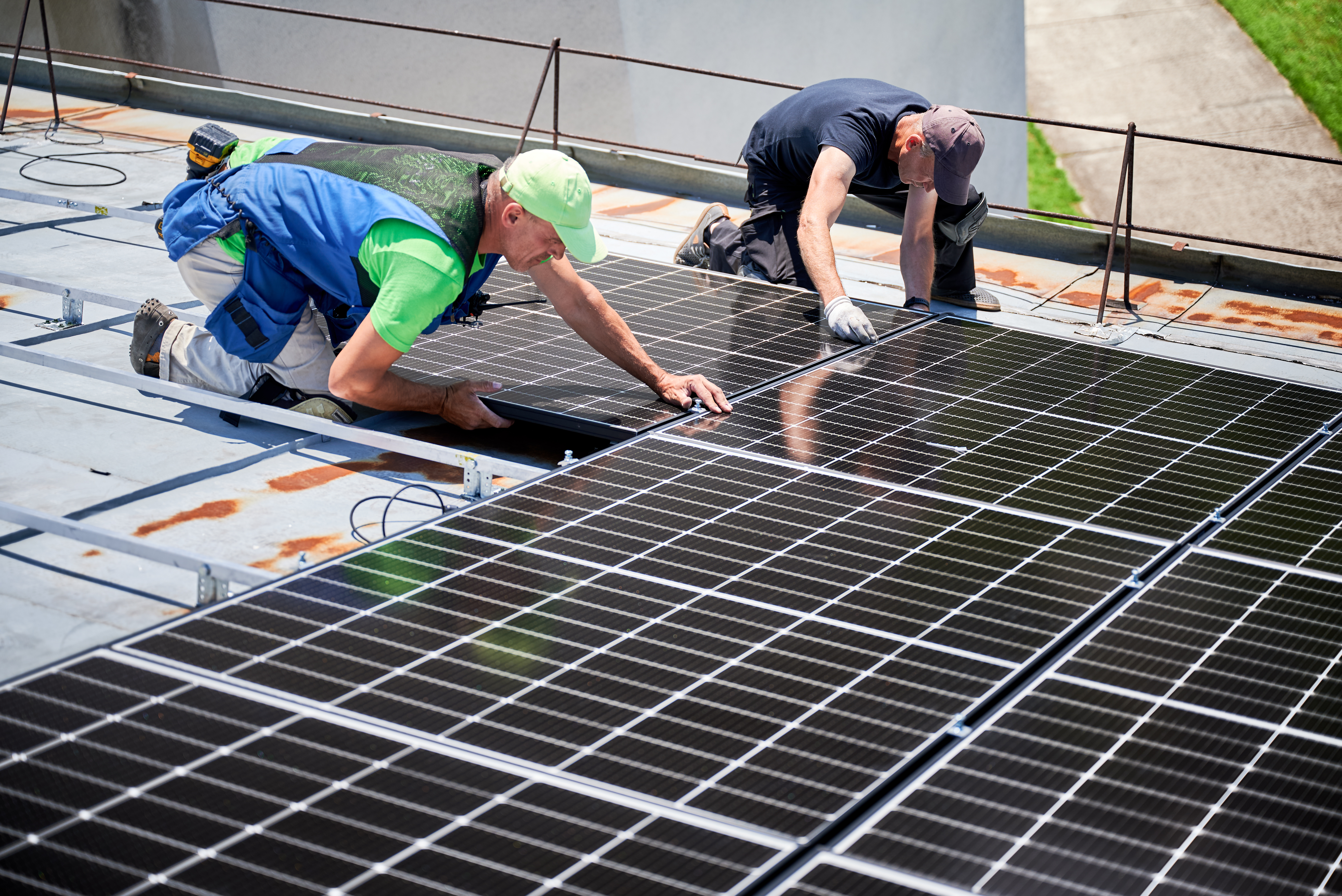 Workers building solar panel system on metal rooftop of house. Two men installers installing photovoltaic solar module outdoors. Alternative, green and renewable energy generation concept.